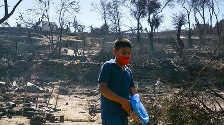 Ein Junge trägt einen Mundschutz und hält eine Plastiktüte als er zwischen Trümmern in einem beschädigten Bereich im Flüchtlingslager Moria geht