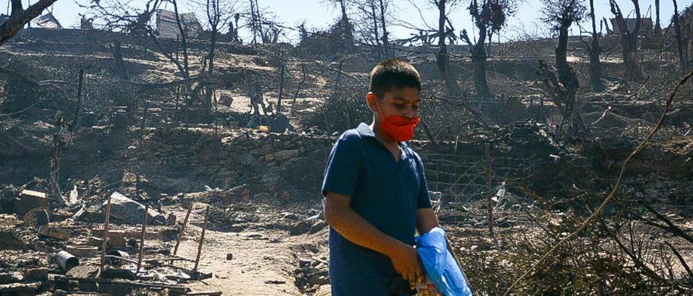 Ein Junge trägt einen Mundschutz und hält eine Plastiktüte als er zwischen Trümmern in einem beschädigten Bereich im Flüchtlingslager Moria geht