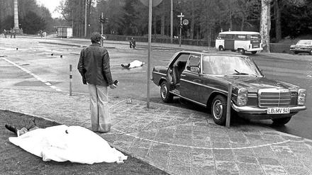 Der Tatort mit den zugedeckten Leichen von Siegfried Buback (vorne links) und seines Fahrers sowie der Dienstwagen des Generalbundesanwaltes, aufgenommen am 07.04.1977.