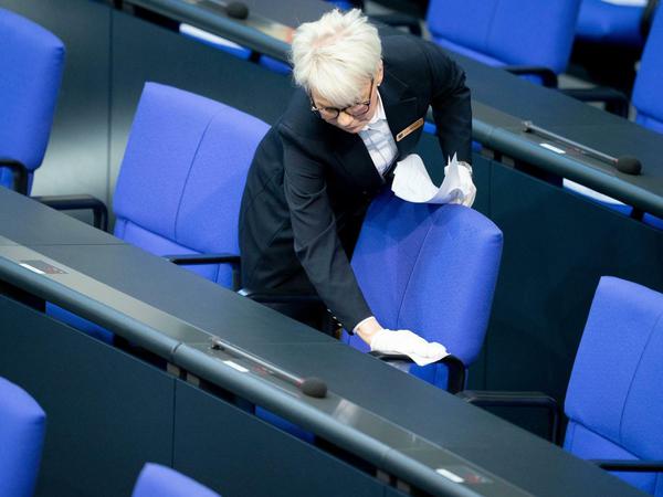 Eine Saaldienerin des Bundestages reinigt Tische und Stühle der Regierungsbank. 