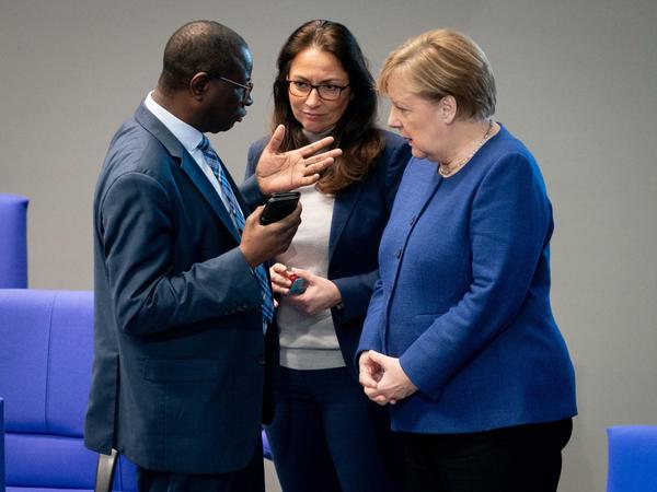 Karamba Diaby mit Bundeskanzlerin Angela Merkel (CDU, r) und der SPD-Politikerin Yasmin Fahimi im Bundestag.