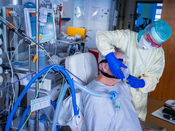 Eine Krankenschwester setzt einem Corona-Patienten auf der Intensivstation eine Beatmungsmaske auf.