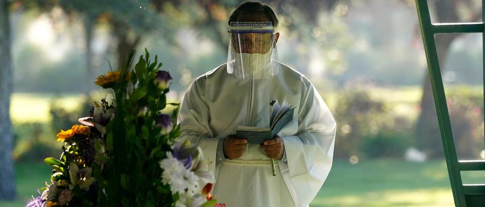 Ein Priester mit Gesichtsschutz nimmt an der Beerdigung einer Person teil, die an Covid-19 gestorben ist. 