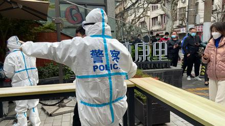 Polizeibeamte in Schutzkleidung führen Anwohner, die sich für Corona-Tests in Shanghai anstellen. 