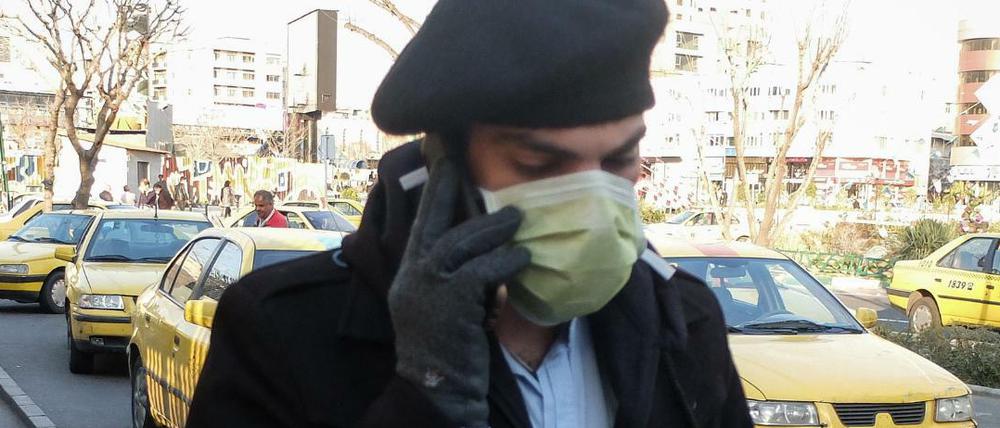 Ein Mann trägt Mundschutz und Handschuhe während er telefonierend eine Straße entlang geht.