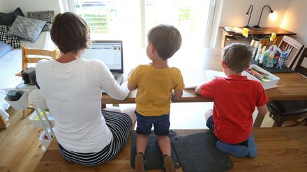 Die Mutter des sechsjährigen Jakob und des vierjährigen Valentin arbeitet Zuhause an einem Laptop, während ihre Kinder neben ihr malen und ein Buch ansehen. 