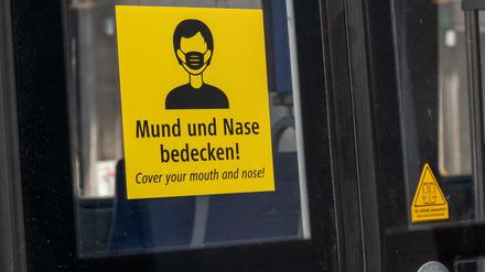 Ein Aufkleber mit der Aufforderung, Mund und Nase zu bedecken, ist in deutscher und englischer Sprache an einer Trambahn in München angebracht. 