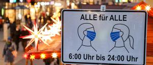 Passanten in Leipzig gehen hinter einem Schild entlang, das auf die Maskenpflicht in der Fußgängerzone hinweist.