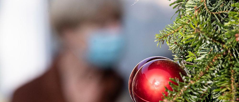 Passantin mit Mund- und Nasenmaske geht hinter einer Weihnachtsbaumkugel vorbei.