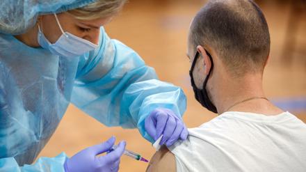 Eine Mitarbeiterin des Gesundheitswesens injiziert einem Mann in einem Impfzentrum einen Corona-Impfstoff. 