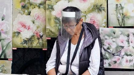 Eine Frau sitzt in Kiew mit einem Gesichtsschild neben gemalten Bildern. 