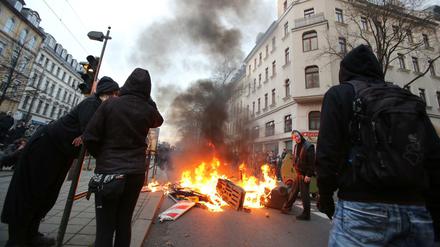 Linke Gegendemonstranten stehen am Samstagabend in Leipzig an einer brennenden Barrikade bei Auseinandersetzungen mit der Polizei. 