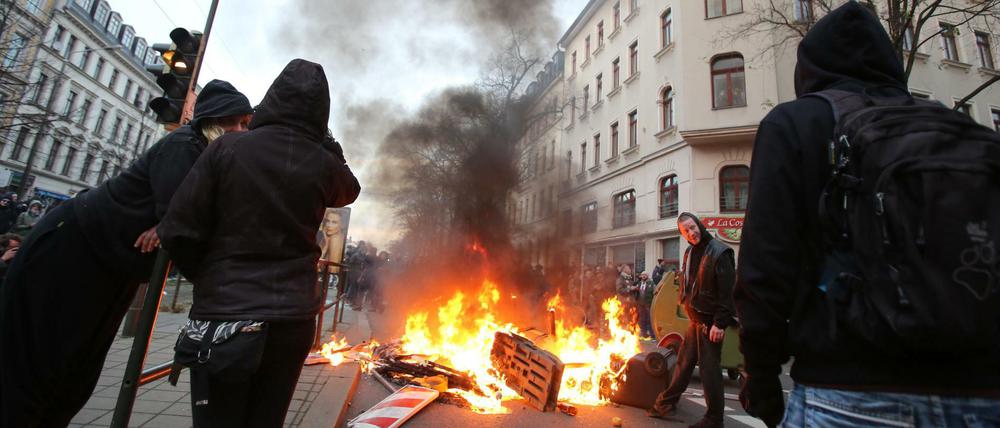 Linke Gegendemonstranten stehen am Samstagabend in Leipzig an einer brennenden Barrikade bei Auseinandersetzungen mit der Polizei. 