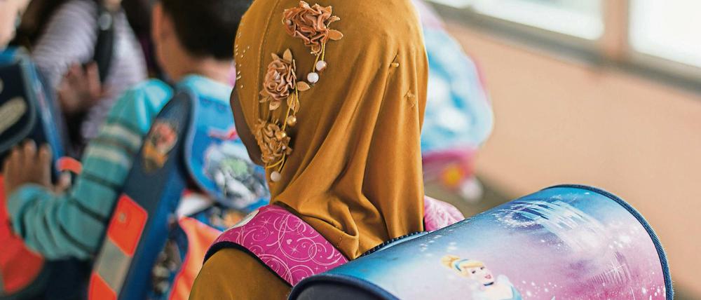 Ein Mädchen mit Kopftuch steht 2015 in einer Schule vor einem Klassenzimmer. 