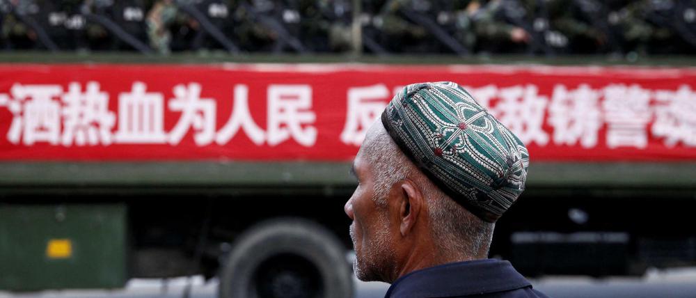 Ein Uigure vor einem Wagen mit Polizeikräften 