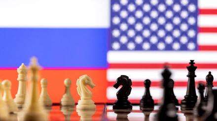 Das Bild zeigt Schachfiguren und im Hintergrund die Fahnen Russlands und der USA. 