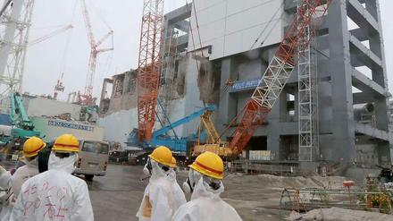 Arbeiter in Schutzanzügen stehen im Juni 2013 vor der Reaktorruine von Fukushima. Bei der Katastrophe starben 2011 über 20.000 Menschen.