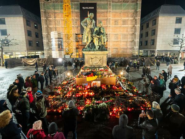 Menschen stehen um das Brüder-Grimm-Denkmal in Hanau, an dem zum Gedenken Blumen niedergelegt wurden.
