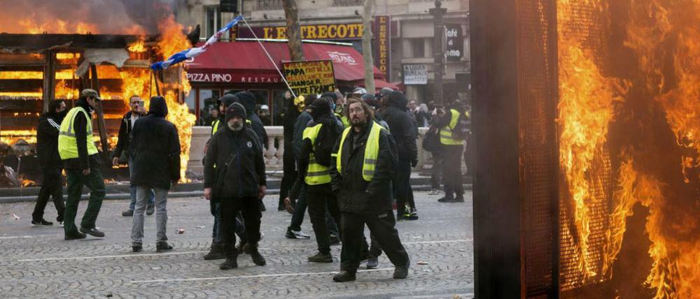 Krawall in Paris: Demonstranten der "Gelbwesten" stehen inmitten von brennenden Objekten und Rauchschwaden.
