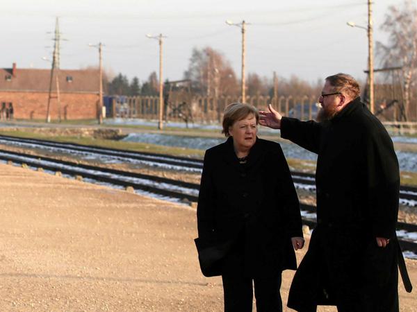 Angela Merkel hört dem Historiker Piotr Cywinski zu.
