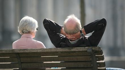 Ein Rentnerpaar sitzt auf einer Bank vor dem Reichstag und sonnt sich. 