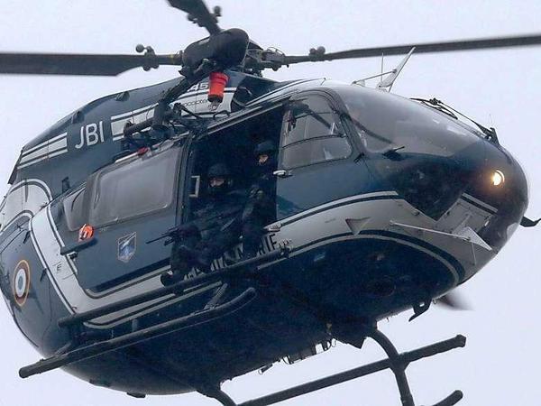 Mit vorgehaltener Waffe sitzen Polizisten im offenen Helikopter über Dammartin.