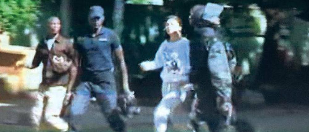 Bloß weg hier! Das von einem Bildschirm abfotografierte Foto eines Videos zeigt aus dem Hotel fliehende Geiseln, die von Sicherheitskräften begleitet werden. 