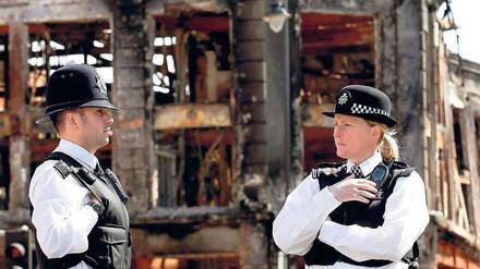 Quer durch London. Polizisten sichern ein ausgebranntes Gebäude im Nordlondoner Viertel Tottenham. Schäden nach Randale gab es auch in Brixton südlich der Themse. Fotos: dpa