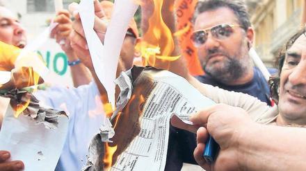 Weg damit. Empörte Staatsbedienstete verbrennen Steuerbescheide vor dem Finanzministerium in Athen. Sie wehren sich gegen eine Sondersteuer. Foto: Orestis Panagiotou/dpa