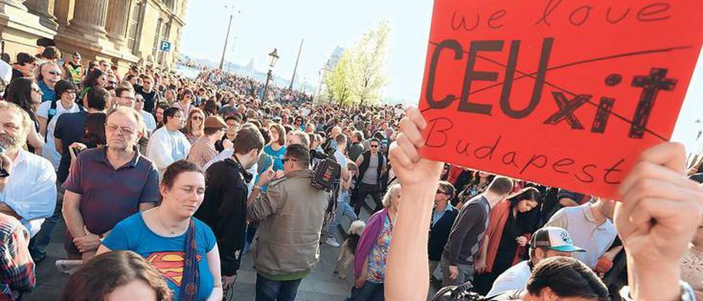 Ein Mann hält bei einer Demonstration ein Plakat mit der Aufschrift "CEUxit" hoch. Der Schriftzug ist durchgestrichen und durch die Worte "We love Budapest" ergänzt.