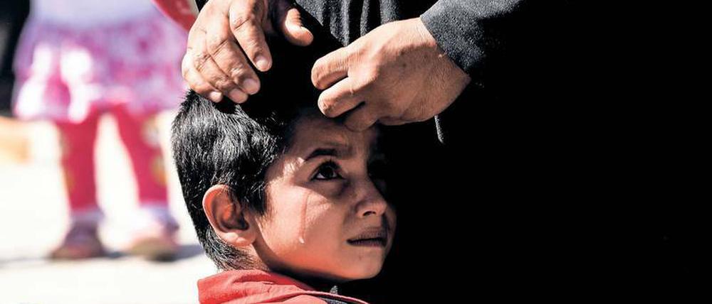 Ein weinendes Kind schmiegt sich an einen Erwachsenen, dessen Hände liegen auf dem Kopf des Kindes.