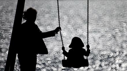 Eine Mutter schaukelt ihr Kind auf einem kleinen Spielplatz. (Symbolbild)