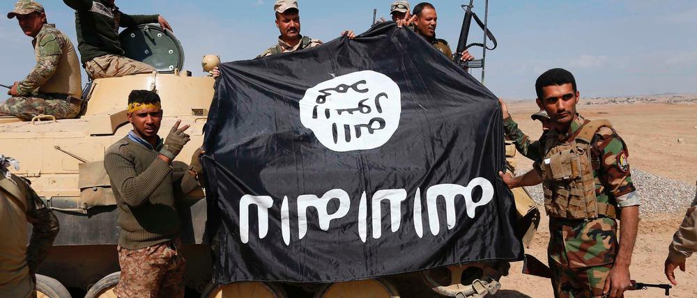 Irakische Soldaten halten eine erbeutete IS-Fahne hoch.
