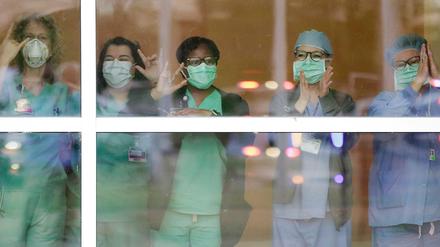 Mit Mundschutz stehen medizinische Mitarbeiter hinter einer Glasscheibe