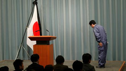Der japanische Premierminister verbeugt sich vor Beginn einer Pressekonferenz vor der mit Trauerflor geschmückten Nationalflagge.
