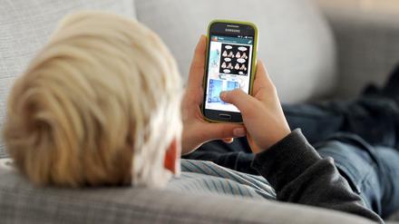 Ein Kind liegt auf einem Sofa und blickt auf sein Smartphone, stundenlang. Derzeit Alltag in vielen Familien.