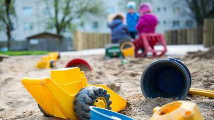 Spielzeug liegt in einem Sandkasten während Kinder in einer Kindertagesstätte spielen.