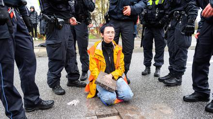 Aktivistin sitzt mit einem Betonteil an ihrer Hand zwischen Polizisten auf der Fahrbahn.