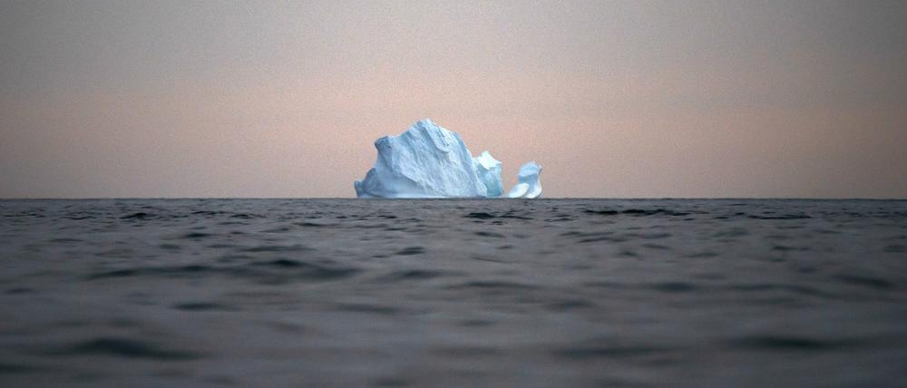 Grönland, Kulusuk: Ein Eisberg schwimmt bei Sonnenuntergang auf dem Meer.