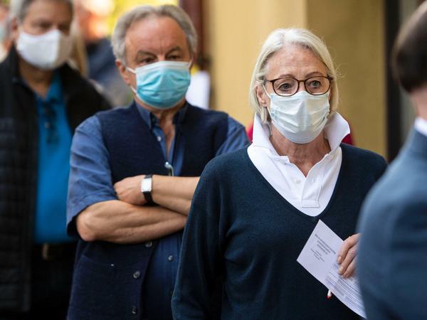 Wählerinnen und Wähler mit Mund-Nasen-Schutz stehen vor einem Wahllokal in Köln an. 