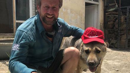 Paul Farthing kniet neben einem Hund, der eine Kappe trägt.