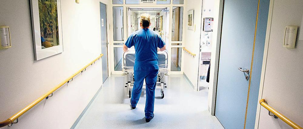 Ein Krankenpfleger schiebt in einer Berliner Klinik ein Krankenbett durch den Flur.