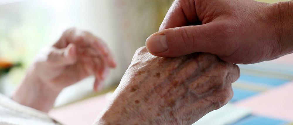 Ein Pfleger hält in einem Alten-und Pflegeheim die Hand einer Bewohnerin.