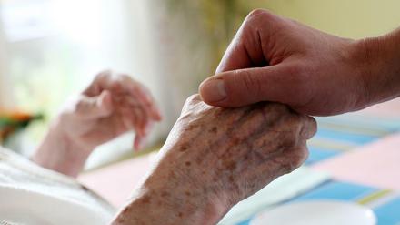Ein Pfleger hält in einem Alten-und Pflegeheim die Hand einer Bewohnerin