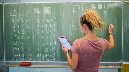 Eine junge Lehrerin schreibt im Matheunterricht an eine Schultafel.