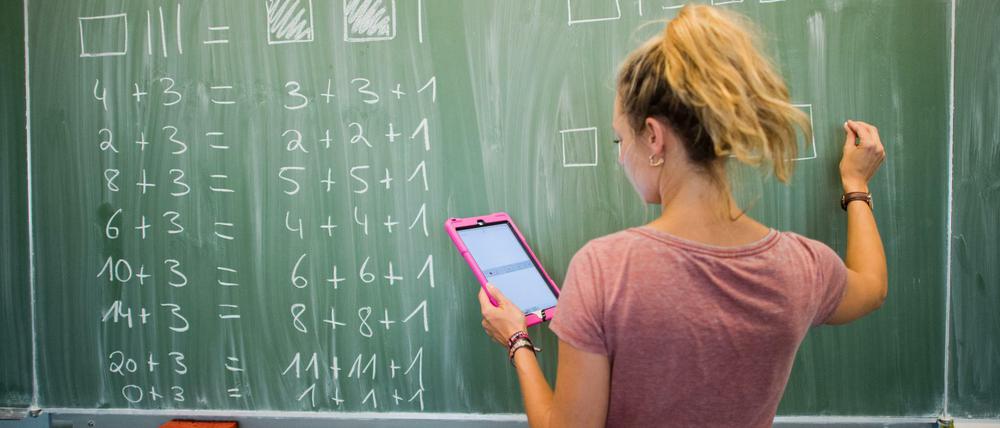 Eine junge Lehrerin schreibt im Matheunterricht an eine Schultafel.