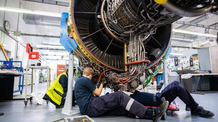 Kurzarbeit. Drei Männer arbeiten in einer Werkstatt von Lufthansa Technik am Triebwerk eines Flugzeuges. 