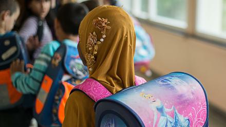 Ein Mädchen mit Kopftuch steht in einer Schule vor einem Klassenzimmer. 