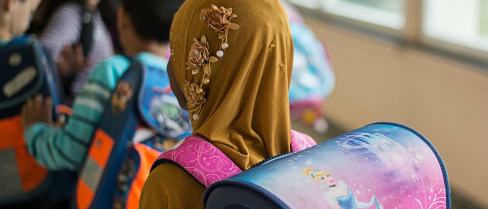 Ein Mädchen mit Kopftuch steht in einer Schule vor einem Klassenzimmer.