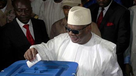 schwarzer Mann mit Sonnenbrille und weißem Gewand wirft Stimmzettel in Urne
